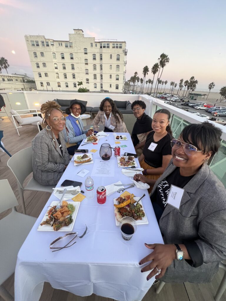 JoC leaders sit at a table on an outdoor patio with a view of the sunset and palm trees in the background